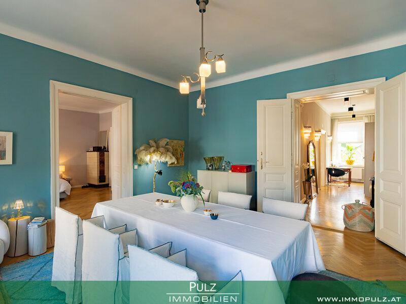 Geräumiges Esszimmer mit Parkettboden, blauen Wänden und Zugang zu weiteren Zimmern.