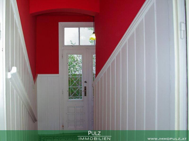 Heller Eingangsbereich mit roter Wandfarbe, weißer Holzvertäfelung und Glastür.
