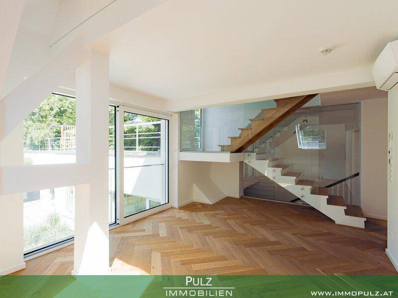 Lichtdurchfluteter Wohnbereich mit offener Treppe, Glasgeländer und großen Fensterfronten.