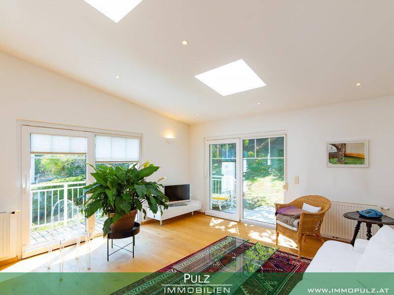 Helles Wohnzimmer mit großen Fenstern, Holzboden und direktem Zugang zur Terrasse.