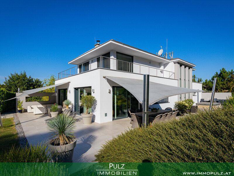 Große, geflieste Terrasse mit Sonnenliegen und Pflanzen, geschützt durch moderne Sonnensegel.
