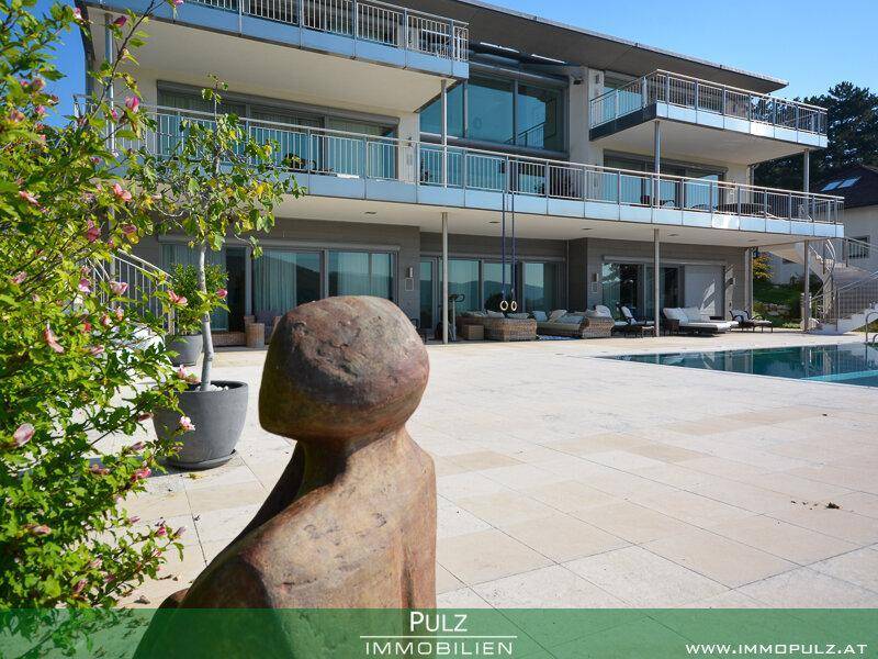 Elegante Villa mit weitläufiger Poolterrasse und moderner Architektur unter blauem Himmel.
