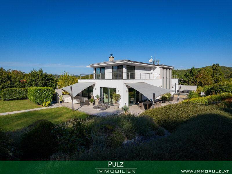 Rückansicht der modernen Villa mit großer Terrasse, Sonnensegeln und gepflegtem Rasenbereich.
