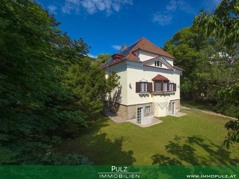 Historische Villa mit klassischer Architektur und weitläufigem Gartenbereich unter blauem Himmel.