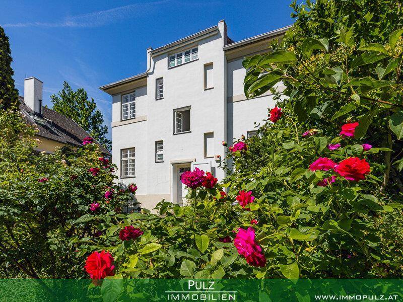 Charmantes weißes Wohnhaus, umgeben von einem blühenden Rosengarten unter strahlend blauem Himmel.