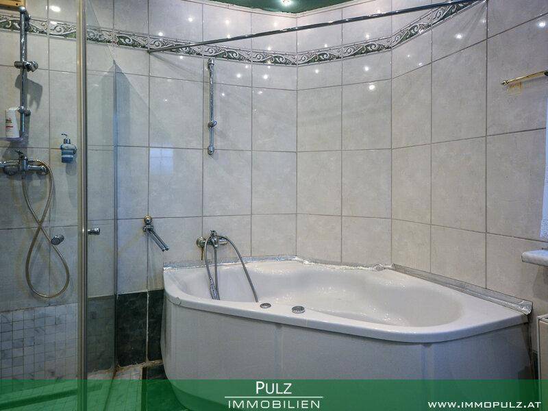 Badezimmer mit Eckbadewanne und Duschbereich, gefliest in Weiß und Dunkelgrün.