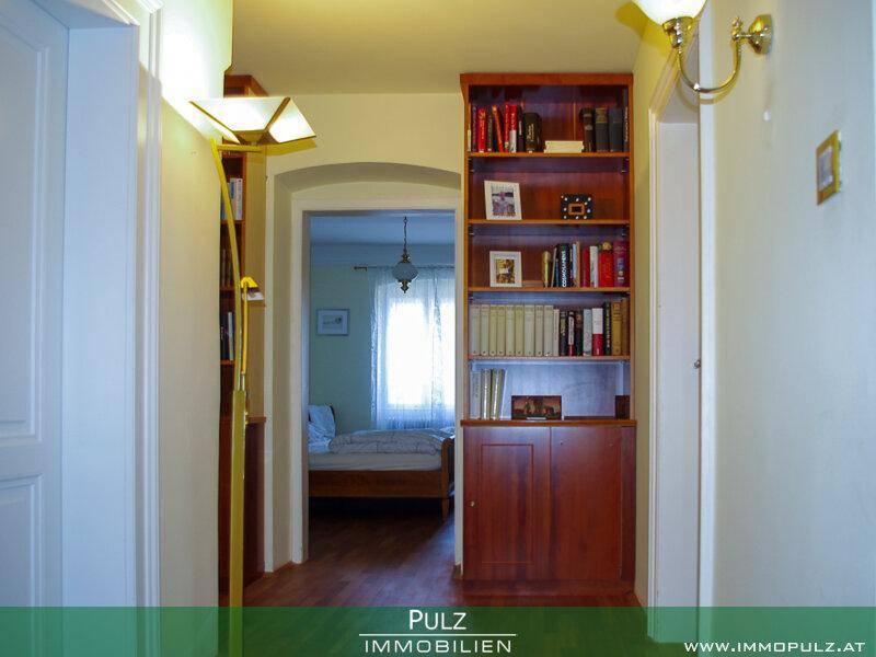 Flur mit Bücherregal und Durchgang zu einem Schlafzimmer mit Holzbett.