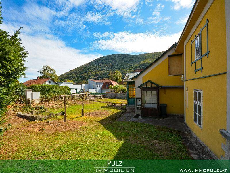 Gelbes Haus mit angrenzendem Gartenbereich, der Potenzial für Gestaltung bietet, unter blauem Himmel.