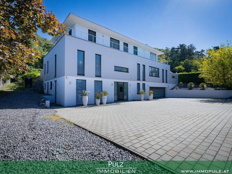 Elegante Frontansicht der modernen Villa mit weitläufiger gepflasterter Einfahrt und Kiesbereich.