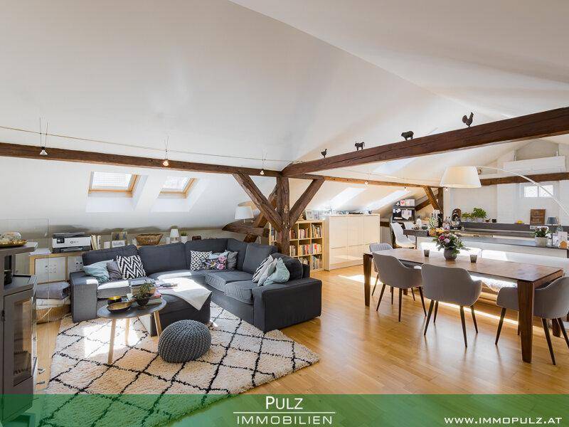 Geräumiger offener Wohn-Essbereich mit Holzbalken, Dachschrägen und modernen Möbeln unter Oberlichtern.