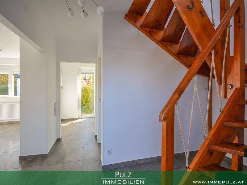 Heller Flur mit Holztreppe und Fliesenboden, der zu weiteren Räumen führt.