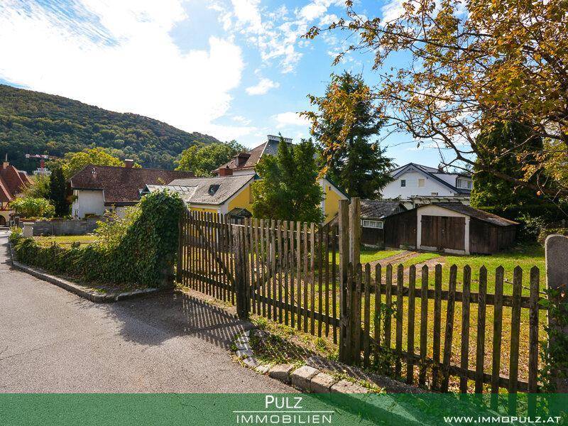 Ländliche Straße mit Holzzaun und Blick auf die umliegenden Häuser und bewaldeten Hügel.