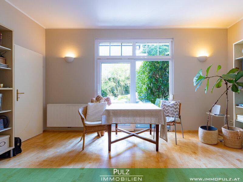Helles Zimmer mit Holzboden, großem Fenster und Blick in den grünen Garten.