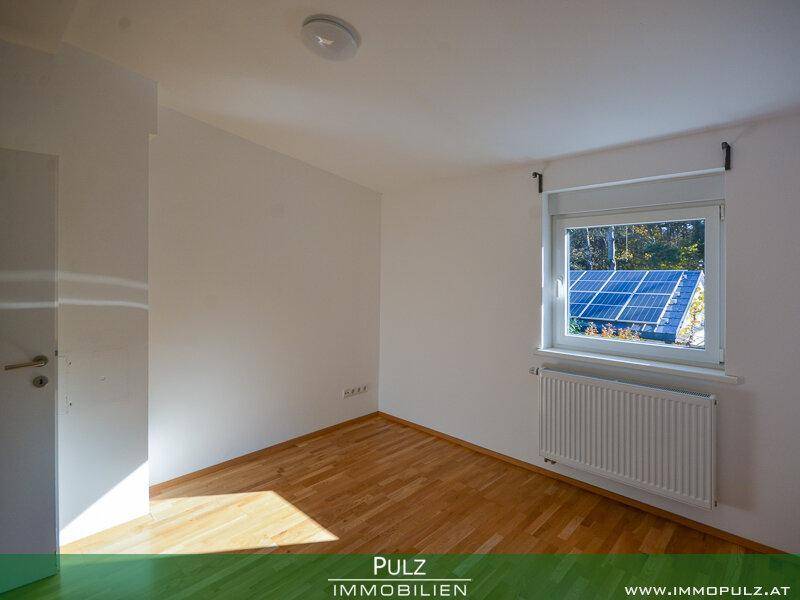Helles Schlafzimmer mit Parkettboden und Blick auf die Photovoltaikanlage.