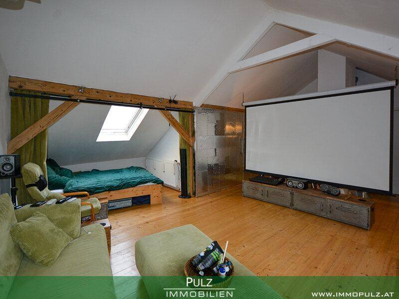 Dachgeschoss-Wohnbereich mit großem Projektionsbildschirm, Holzboden und gemütlichem Sofa.