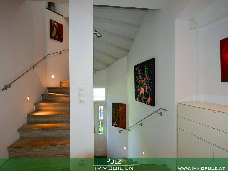Beleuchtetes Treppenhaus mit modernen Wandleuchten und Kunstwerken an den Wänden.