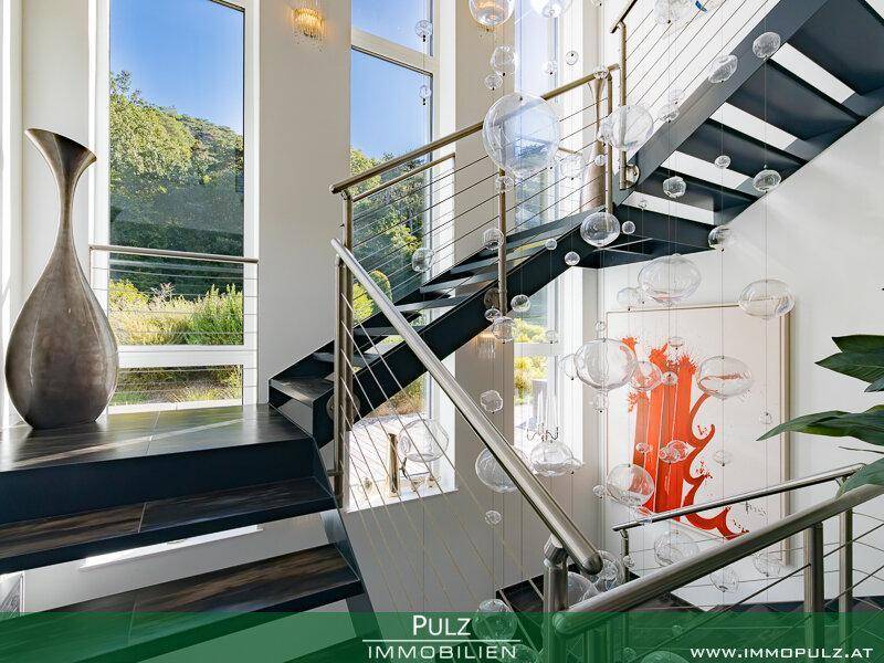 Elegantes Treppenhaus mit modernen Glas- und Metallgeländern und großen Fenstern mit Weitblick.