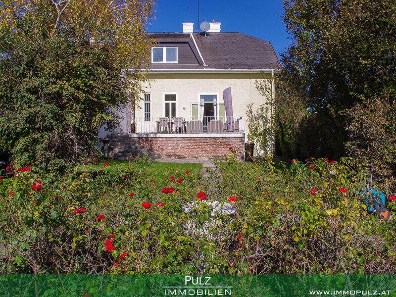 Rückansicht des Hauses mit Terrasse und einem blühenden Rosengarten im Vordergrund.