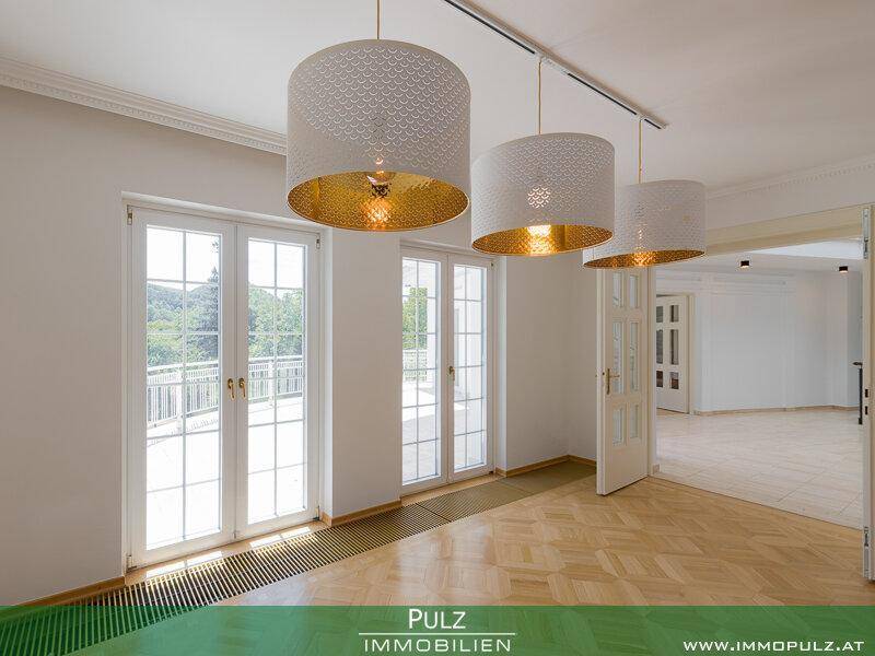 Lichtdurchflutetes Wohnzimmer mit Parkettboden und großen Fenstertüren zum Balkon.