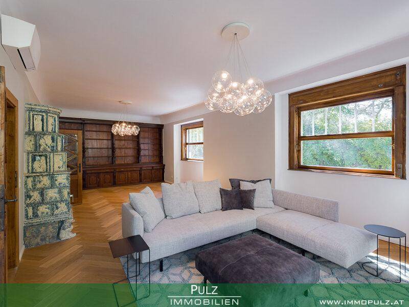 Gemütliches Wohnzimmer mit großem Sofa, Kachelofen und Blick ins Grüne.