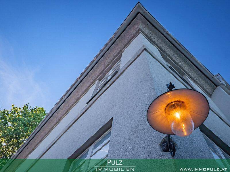 Architektonisches Detail der Hausfassade mit einer klassischen Außenleuchte unter blauem Himmel.