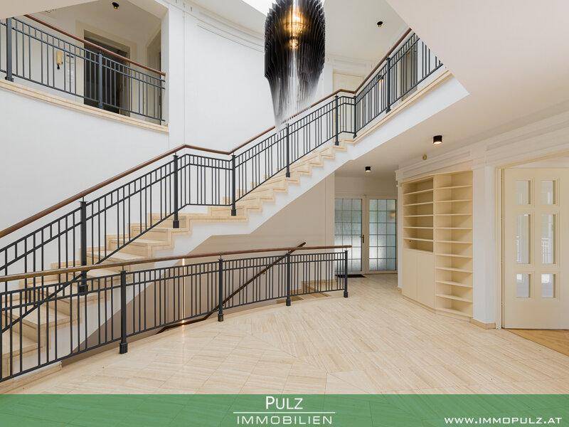 Großzügiges Treppenhaus mit elegantem Geländer, Marmorboden und moderner Deckenleuchte.