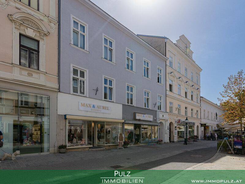 Ansicht einer historischen Straße mit Geschäften und Gebäuden unter strahlendem Sonnenschein.