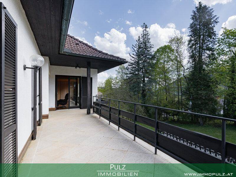 Geräumiger Balkon mit Fliesenboden und Zugang zu Innenräumen, umgeben von Bäumen.