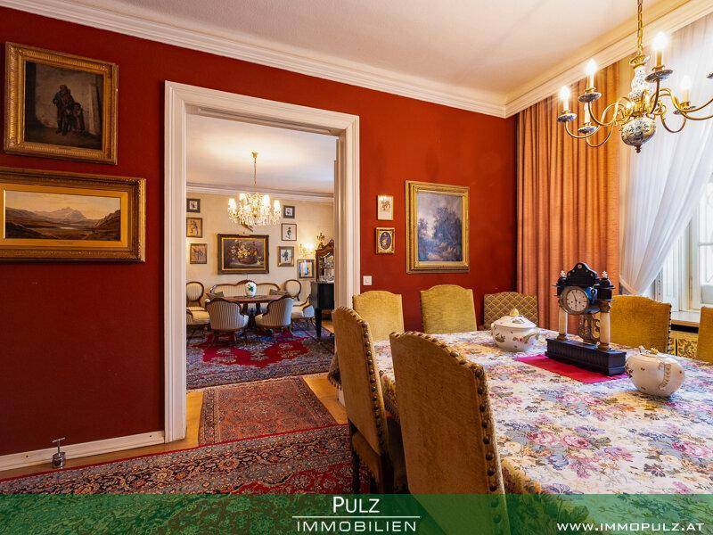 Klassisches Esszimmer mit roter Wandfarbe und Blick in einen weiteren eleganten Wohnbereich.