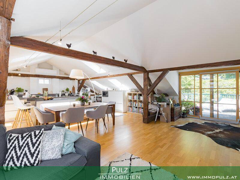 Heller Wohnbereich mit Holzbalken, großem Esstisch und Zugang zu einer Terrasse durch eine Schiebetür.
