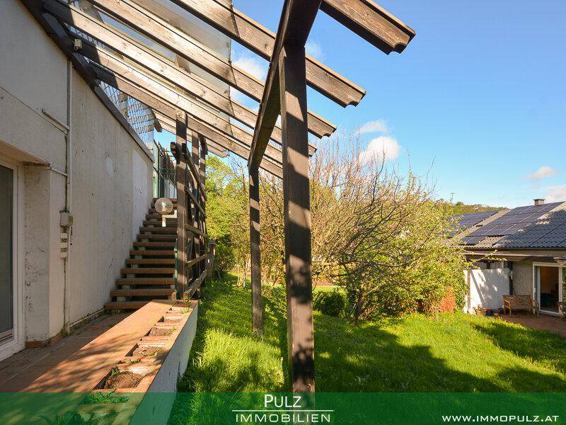 Seitlicher Gartenbereich mit Rasen, Bäumen und einer Holzpergola-Struktur.