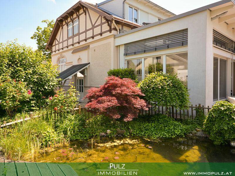 Seitlicher Blick auf das Haus mit üppigem Garten, Ziersträuchern und einem kleinen Teich.