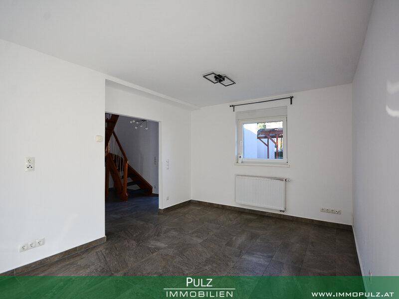 Geräumiger, heller Raum mit Fliesenboden und Blick auf die Holztreppe.