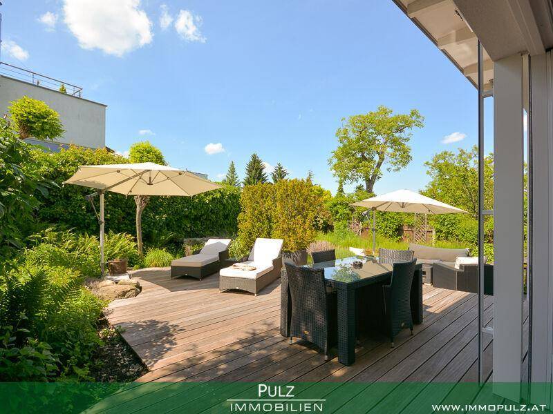 Große Holzterrasse mit Essbereich, Liegestühlen und Sonnenschirmen im Grünen.