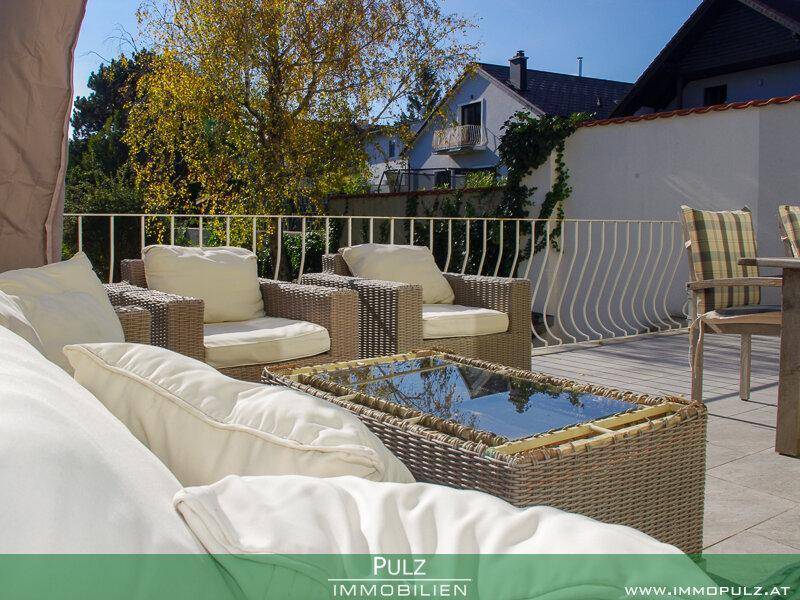 Gemütliche Terrasse mit Rattanmöbeln, Kissen und Blick auf die Umgebung.