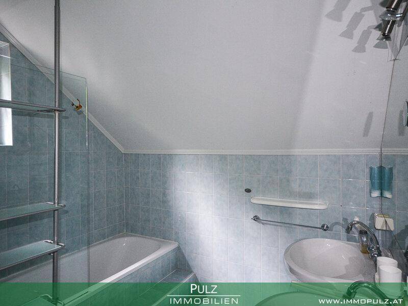 Badezimmer mit blauen Fliesen, Badewanne und Waschbecken unter der Dachschräge.