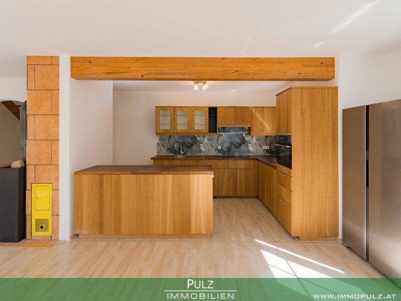 Detailansicht der Holzküche mit Einbaugeräten und großem Kühlschrank im offenen Wohnbereich.