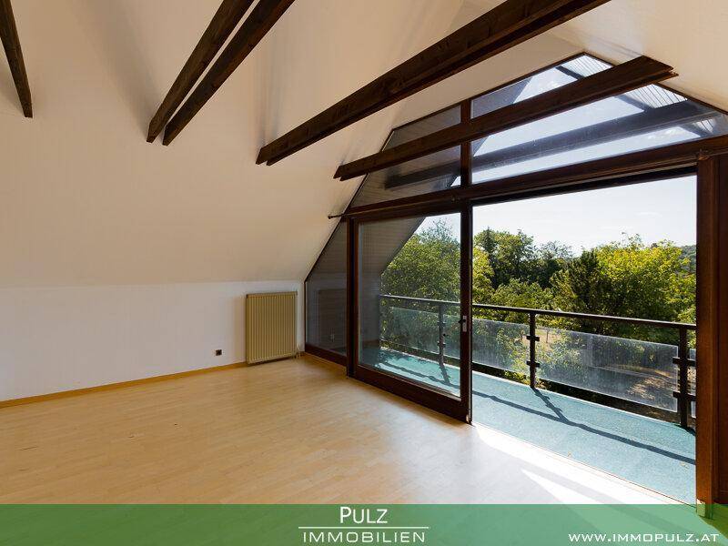 Dachgeschosszimmer mit schräger Decke, Holzbalken und großem Schiebefenster zum Balkon mit Weitblick.