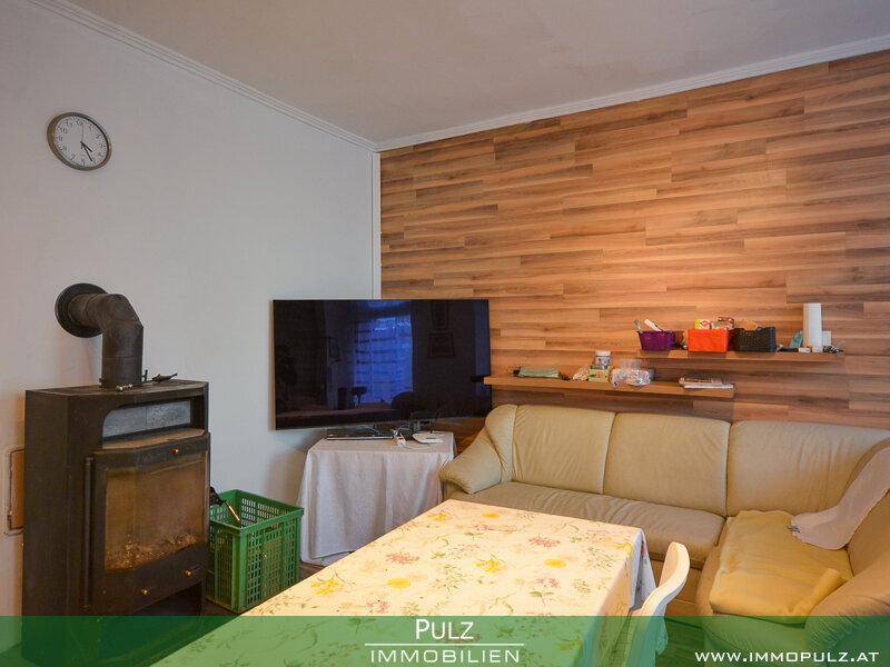 Wohnzimmer mit Holzwandverkleidung, Kaminofen und Sofa, bietet eine warme Atmosphäre.