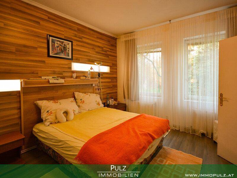 Schlafzimmer mit Holzwandverkleidung, Doppelbett und großen Fenstern für viel Licht.