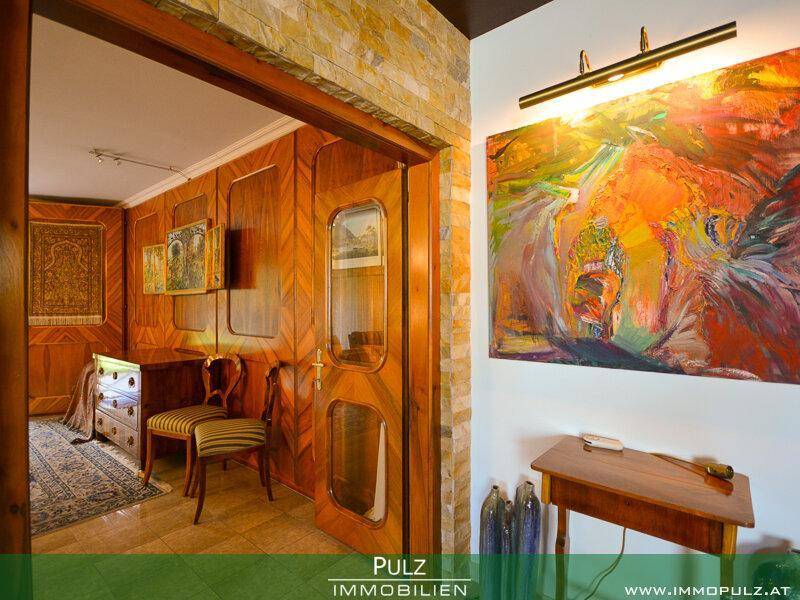 Flur mit Steinwand und Holztür, die zu einem holzvertäfelten Wohnzimmer führt.
