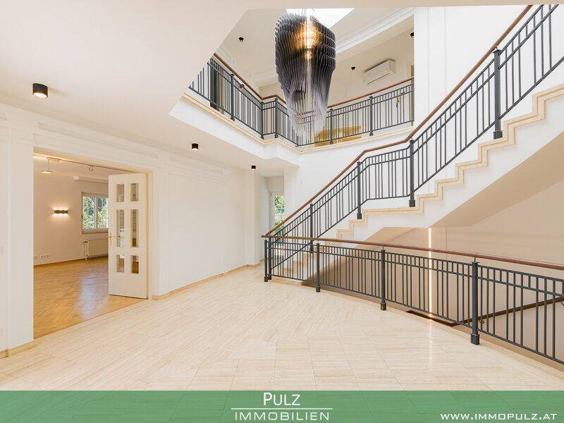 Elegantes Treppenhaus mit geschwungenem Geländer, Marmorboden und Oberlicht für viel Licht.