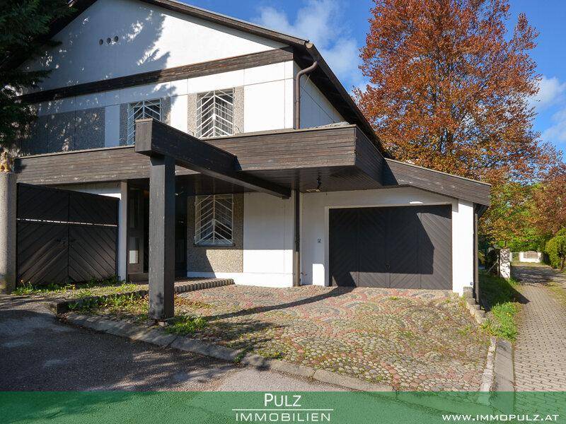Einfamilienhaus mit Carport und Garage, umgeben von Bäumen unter blauem Himmel.