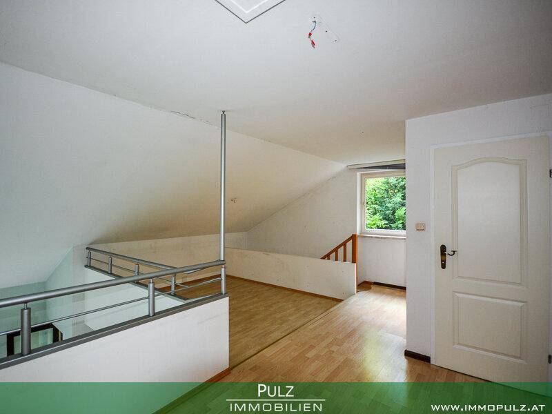 Heller Flur im Dachgeschoss mit Holzfußboden, Schrägen und Geländer.