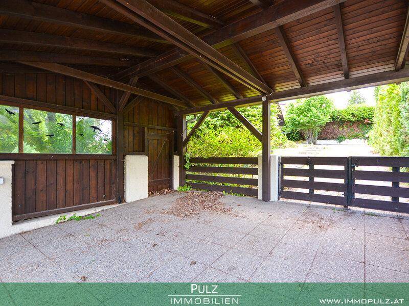 Überdachter Carport oder Abstellbereich mit Holzbalken und gepflastertem Boden.