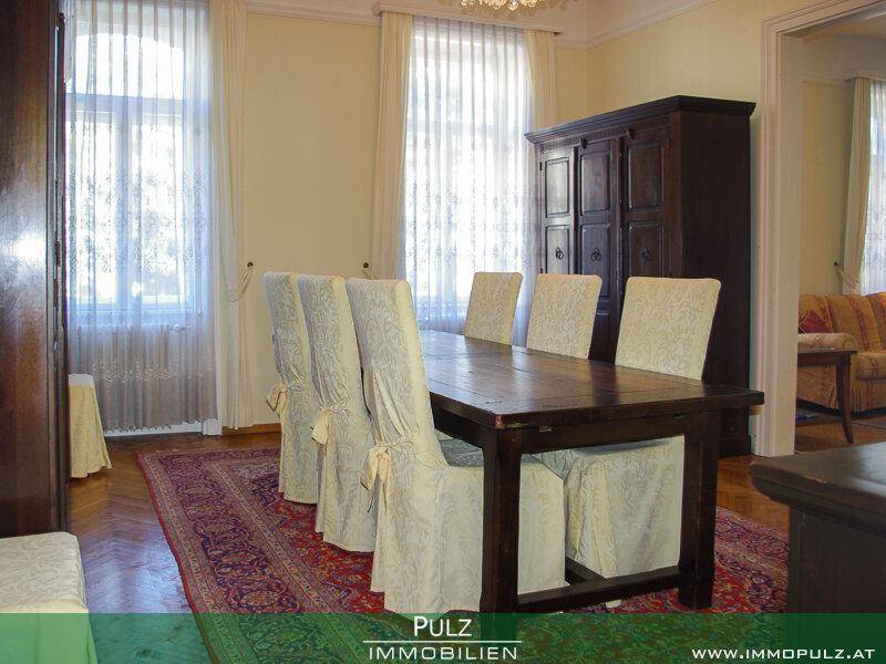 Eleganter Essbereich mit großem Holztisch, Stühlen und einem antiken Schrank.