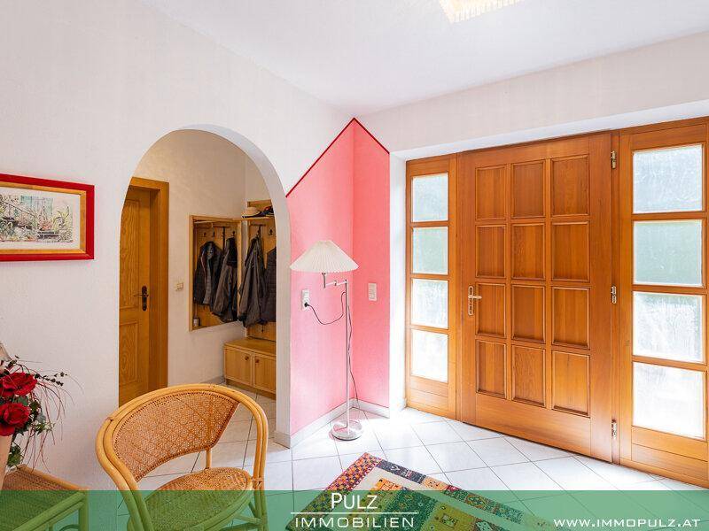 Heller Eingangsbereich mit Holztüren, Fliesenboden und Garderobe, akzentuiert durch eine rosa Wand.