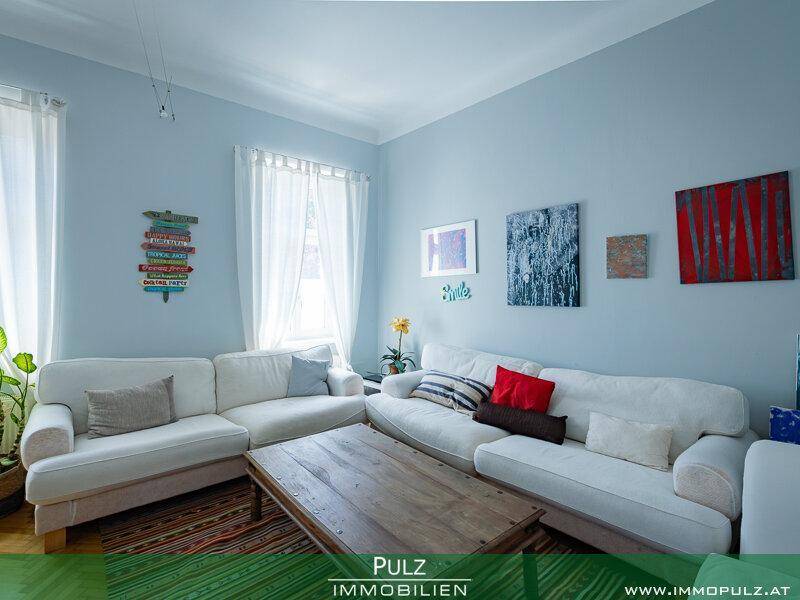 Gemütliches Wohnzimmer mit zwei weißen Sofas, Holztisch und farbenfroher Dekoration an den Wänden.