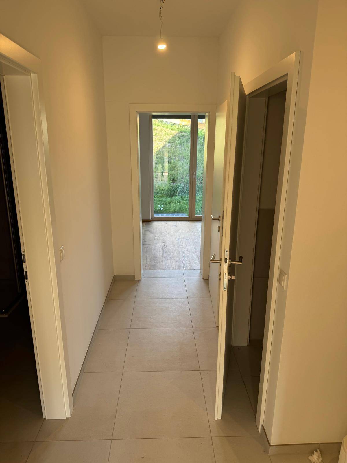 Heller Flur mit Fliesenboden und Zugang zu verschiedenen Zimmern, am Ende ein Fenster.