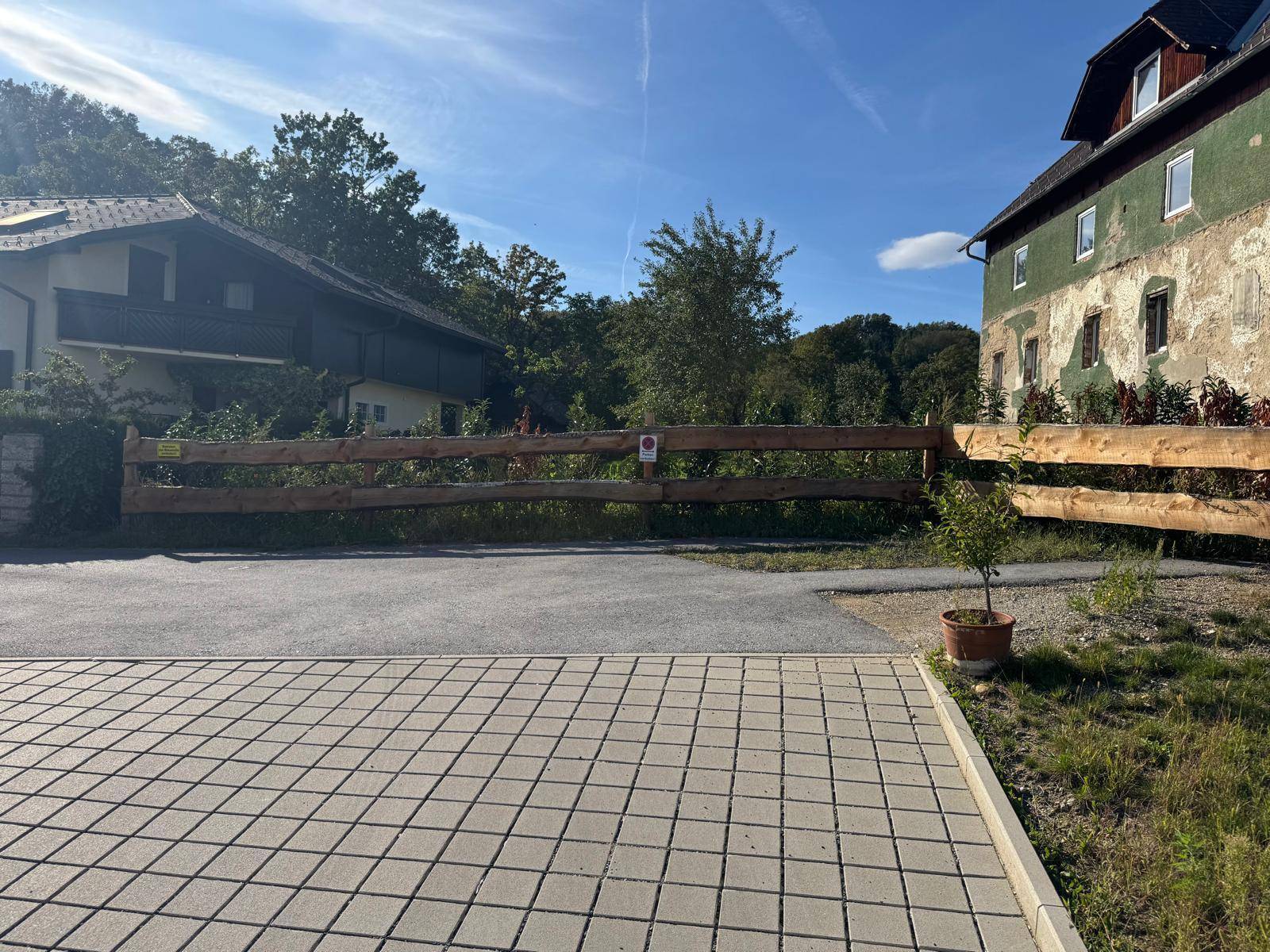 Außenbereich mit gepflasterter Fläche, Zufahrtsstraße und angrenzenden Gebäuden in ländlicher Umgebung.